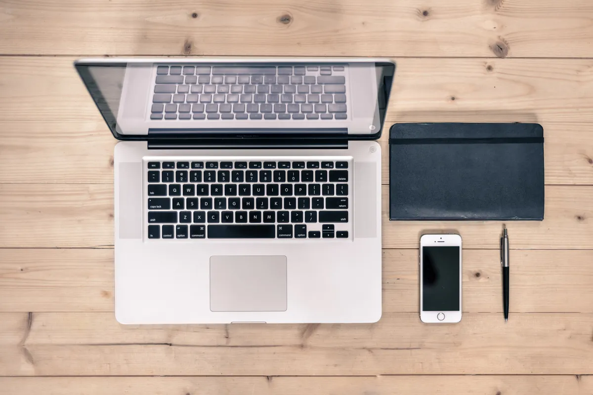 Laptop, phone and notebook side by side on a wooden desk