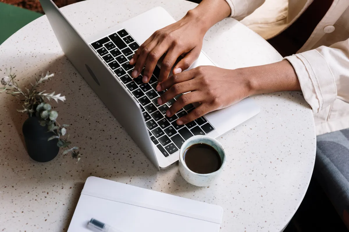 Person typing on a laptop next to a coffee and a notebook